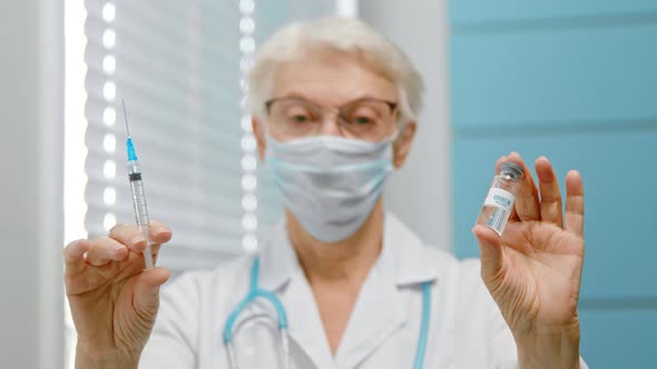 Mature woman doctor with spectacles and disposable mask shows vial of vaccine