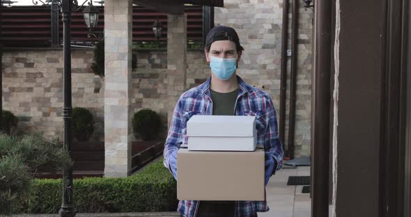 Young Man in Mask and Gloves Looks Confidently and Gives Parcels to Camera