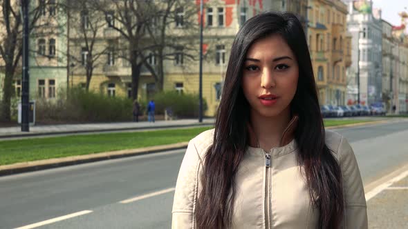 A Young Asian Woman Looks at the Camera in a Street in an Urban Area