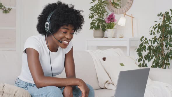 African Attractive Freelancer Woman Wearing Headset Sitting at Home Look Computer Screen Interact