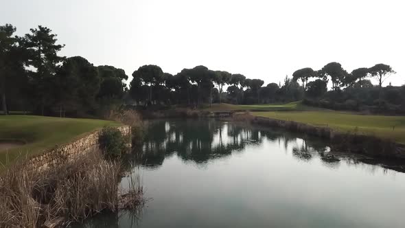 Fast fly over golf course field and pond directly to flag pole