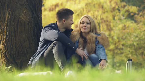 Loving Couple Sitting Under Tree, Having Date Outdoors, Picnic in Park Happiness