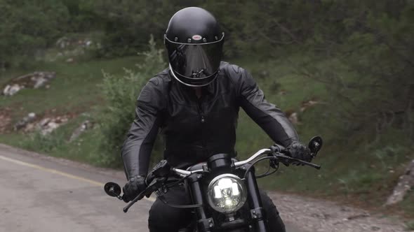 Biker on His Motorcycle Closeup Drives Past on a Asphalt Road in the Middle of a Forest