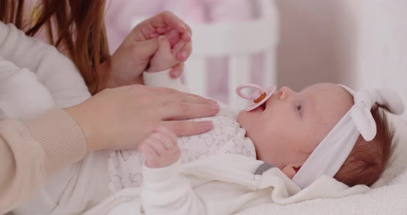 A Young Mother Talks To A Newborn Baby Girl And Kisses Her Tenderly