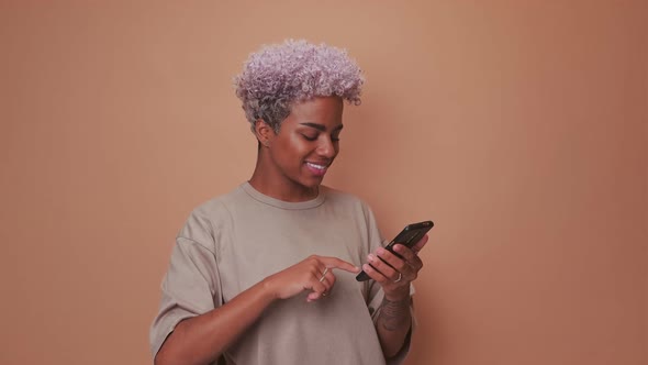 Young African American Woman Uses Mobile Phone and Taps Screen Stands in Studio