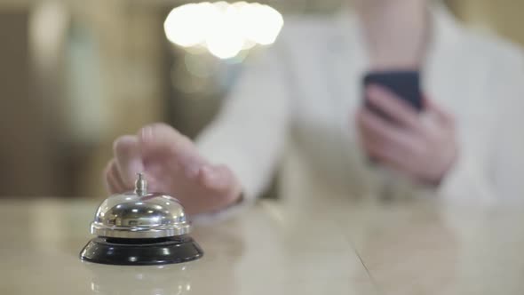 Blurred Caucasian Woman with Smartphone Pressing Hotel Bell at Reception Desk