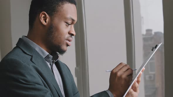 Focused African American Businessman Holding Papers Reading Financial Report Making Notes Standing