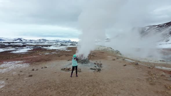 Woman watching geothermal field with fumaroles and geysers. Area with natural steam vents and mud po
