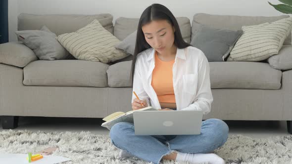 Beautiful asian student studying online and learning, writing notes in a desk at home