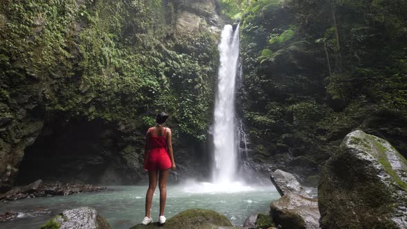 Female Tourist Standing at the Foot of a Waterfall Enjoying the Scenery.