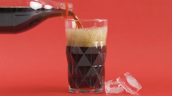 Pouring a cola drink into a glass with ice cubes on the side.