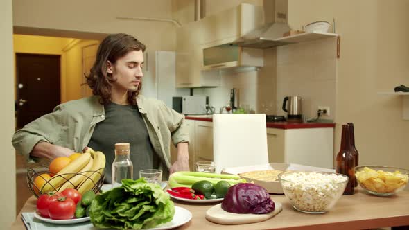 One of Friends is Sitting Down at the Table While His Pal is Entering the Kitchen