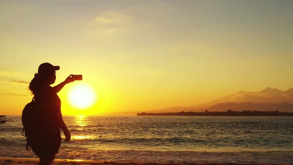 Silhouette of young woman taking photos of beautiful sunset with yellow misty sky reflecting on sea