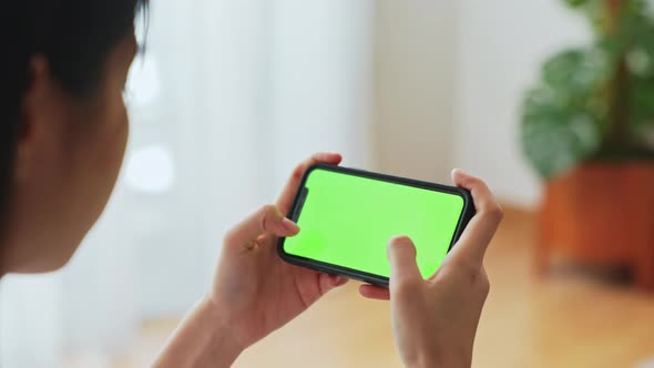 Woman holding in hands a mock up smartphone with green screen for playing games.