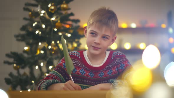 Happy Child Boy Writing Letter To Santa Claus Home Near Christmas Tree