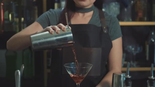 Pretty bartender pouring craft cocktail into martin glass, dolly shot.