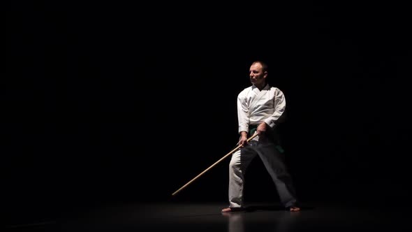 Kendo Fighter on White Kimono Practicing Martial Art with the Bamboo Bokken on Black Background