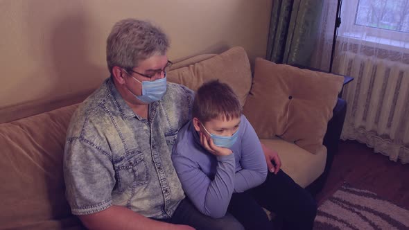 Relaxed Man Resting on the Sofa with His Son in Medical Masks