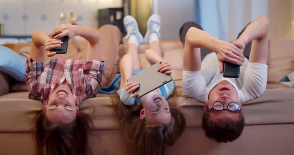 Young Family Relaxing on Couch Upside Down Using Gadgets