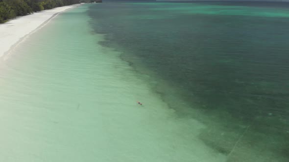 Aerial: woman swimming in turquoise water at sunset white sand beach tropical 