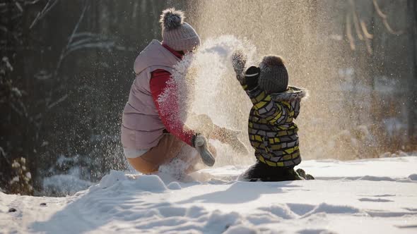 Happy Mother with Little Son Playing with Snow Throwing It Up