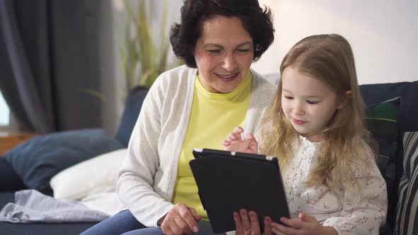 Little Girl Is Showing To Senior Woman New Fun Cyber Game on Tablet