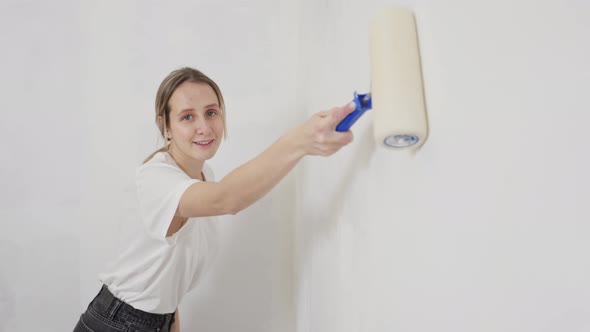 Young Cheerful Woman Paints a Wall at Home with a Paint Roller