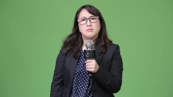 Mature Sad Asian Businesswoman As Newscaster Using Microphone