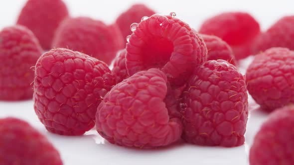 Extreme close up Water drops falling over raspberries lying on white Surface, Slow motion