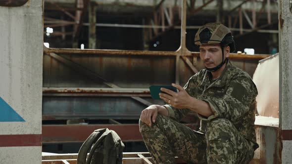 Soldier Having Video Call on Mobile Among Destroyed Plant