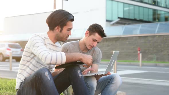 two young multiethnic men sitting outdoor using digital tablet and personal computer