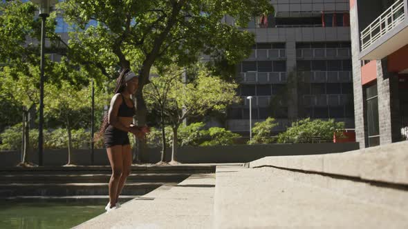 African american woman wearing wireless earphones exercising outdoors jumping on stairs in the city