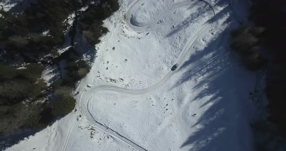 Aerial drone view of man driving his car on a snow covered icy road in the mountains in the winter.