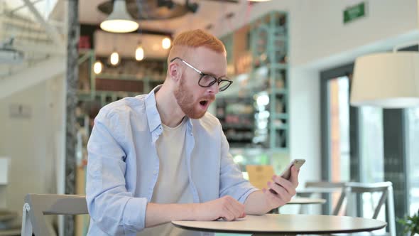 Redhead Man Reacting To Loss on Phone in Cafe 