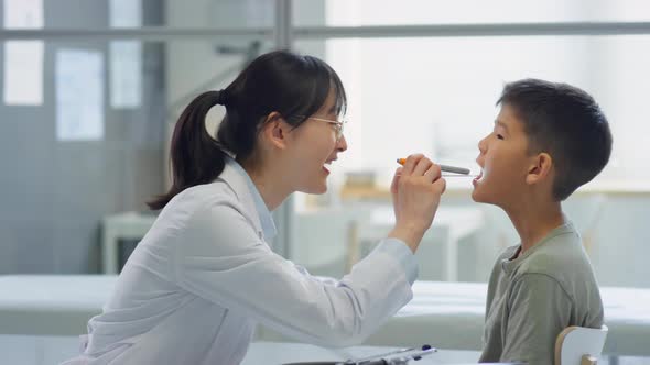 Female Doctor Examining Throat of Asian Tween Boy