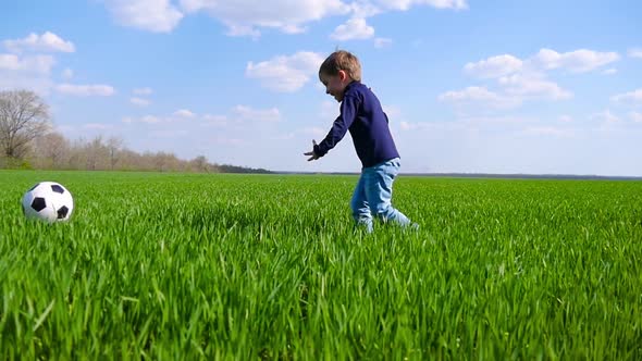 A Happy Child Runs Across a Field of Green Grass and Kicks a Soccer Ball in Slow Motion