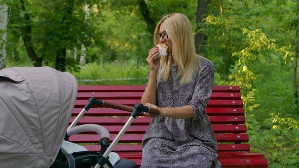 Young Mother Rocking Stroller Sitting Bench Park Eating Burger