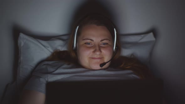 Cheerful Stout Young Woman Making Video Call on Laptop in Bed