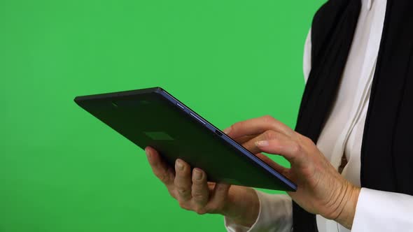 An elderly woman works on a tablet - closeup on the hands from the side - green screen studio