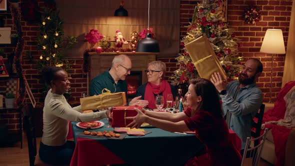 Joyful People Gathered at Christmas Dinner Table While Exchanging Gifts