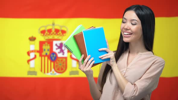 Asian Girl Showing Copybooks Against Spanish Flag Background, Learning Language