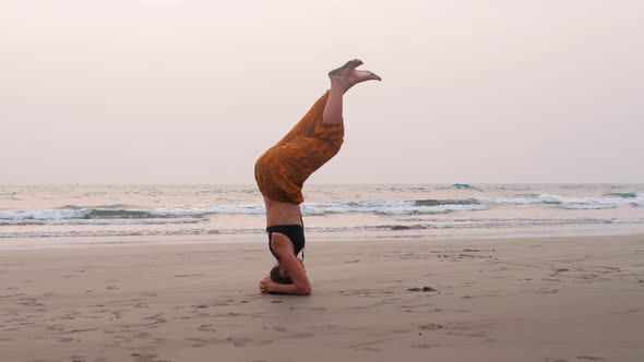 Serenity and Yoga practicingIs on the Head Woman Near Ocean Doing Headstand Upside Down