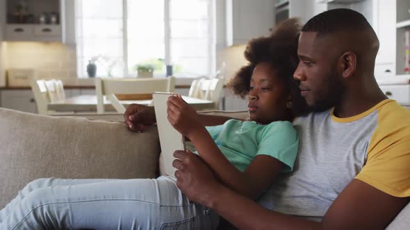 African american daughter and her father using tablet together sitting on couch