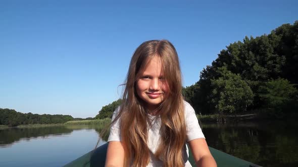 Little Smiling Girl Rowing Along the River and Looking at Camera