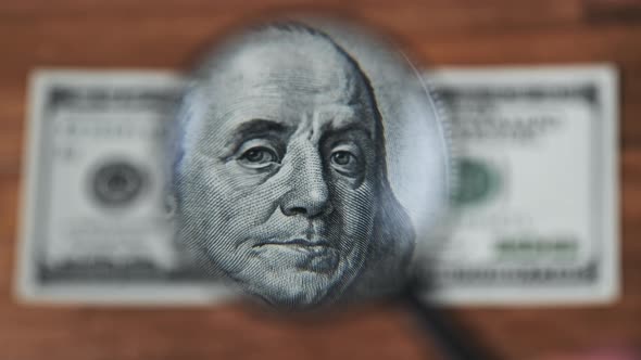 One Hundred Dollars Inspects Under Magnifying Glass on Wooden Table