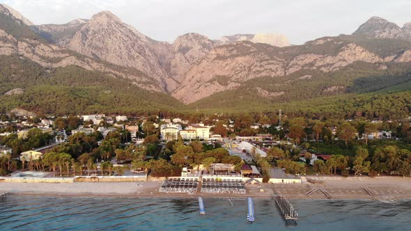 Aerial View of a Small Resort Town on the Mountainous Seaside and Rows of Sun Loungers on the Beach