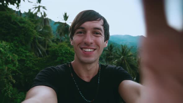 Portrait of Smiling Young Man Tourist Making a Selfie Video on Green Jungle Forest and Palms