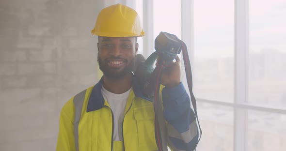 Portrait of Smiling Afroamerican Builder in Uniform Holding Drill on His Shoulder