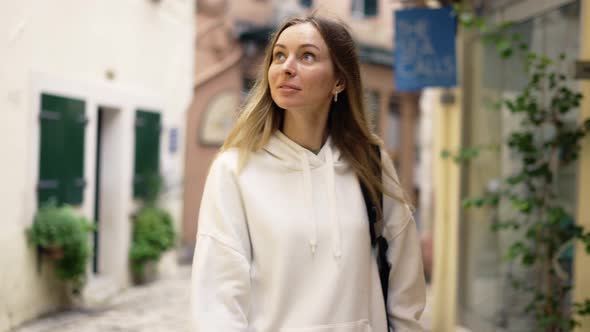 A Woman Walks Along a City Narrow Street with Backpack and Smiling