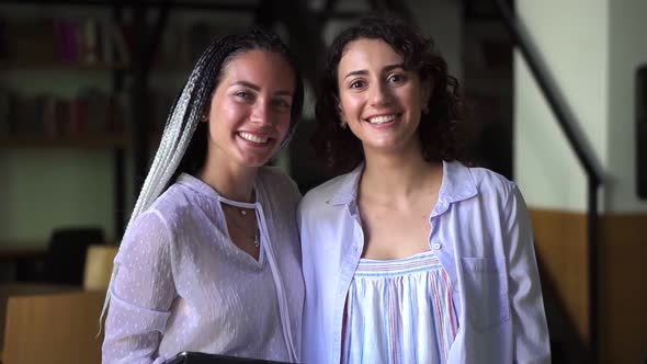 Portrait of Two Pretty Young Caucasian Women in White Blouses Standing in Library and Smiling in